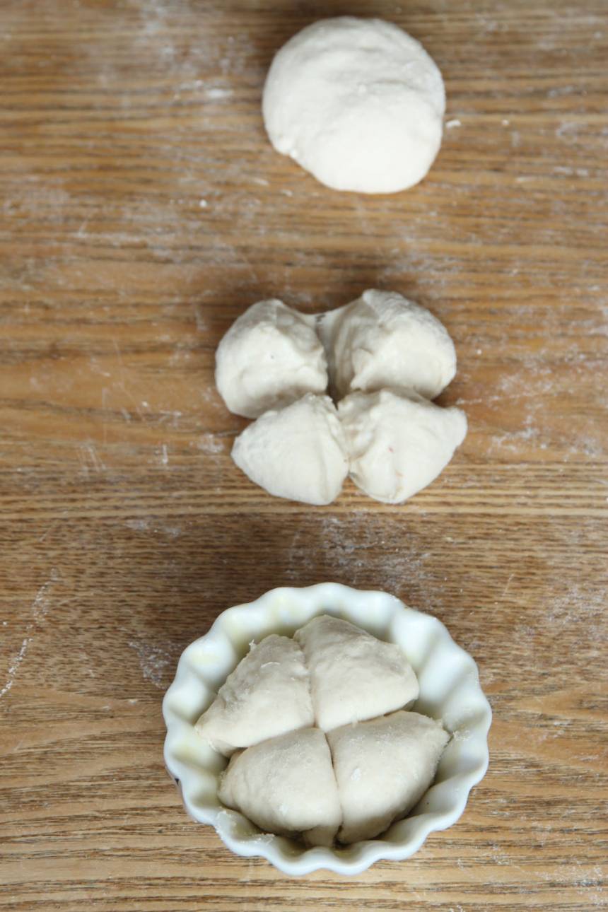 2. Dela degen i 30–34 bitar. Forma runda bullar och skär ett kryss i dem. Lägg dem i muffinsformar av porslin (behöver smörjas) eller papper (behöver inte smörjas). Ställ formarna på en ugnsplåt. Det går också bra att lägga bullarna direkt på en plåt med bakplåtspapper. Låt bröden jäsa under bakduk i ca 30 min. Sätt ugnen på 250 grader.