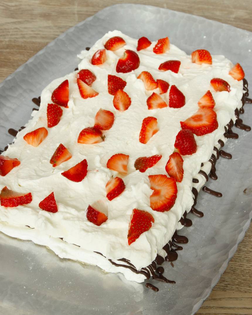 5. Bred ut hälften av grädden på bottnen. Skär hälften av jordgubbarna i småbitar och strö dem över grädden.