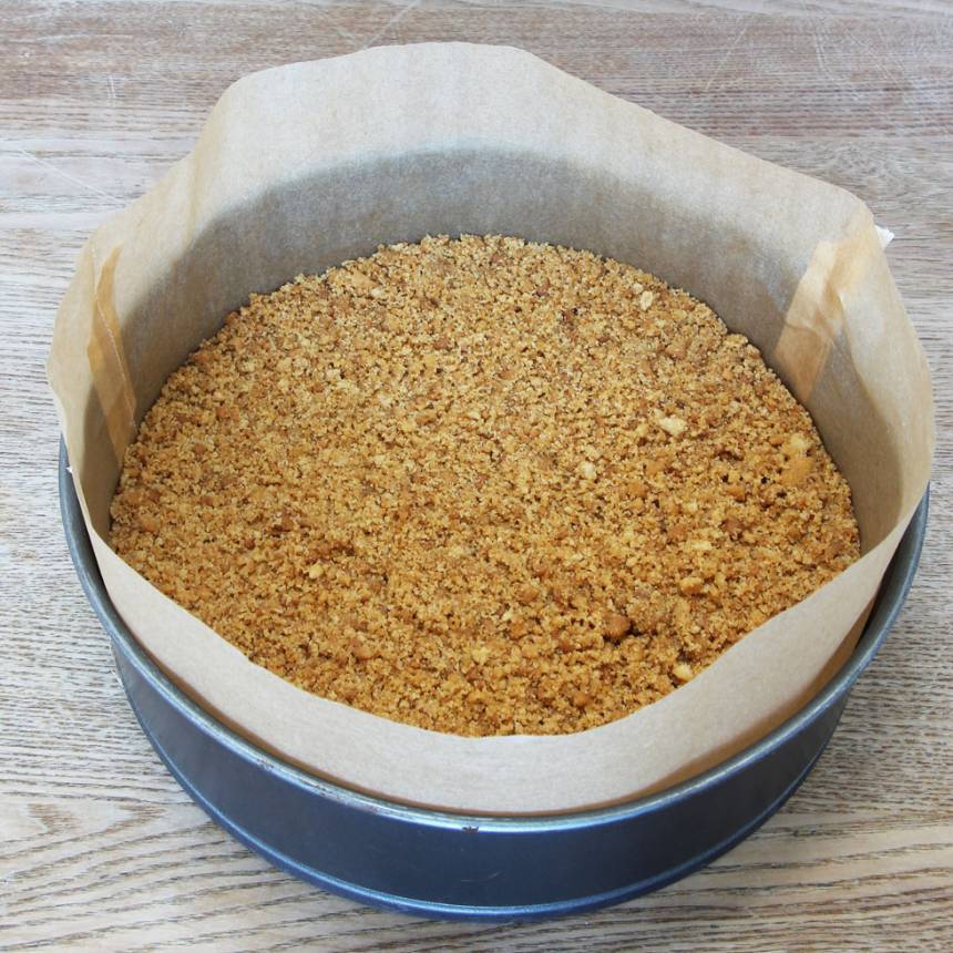2. Tryck fast ett bakplåtspapper i en springform, 23–24 cm i diameter. Klipp en bred remsa bakplåtspapper och klä kanten med det. Tryck ut smulorna i bottnen. Ställ formen i frysen i ca 20 min.