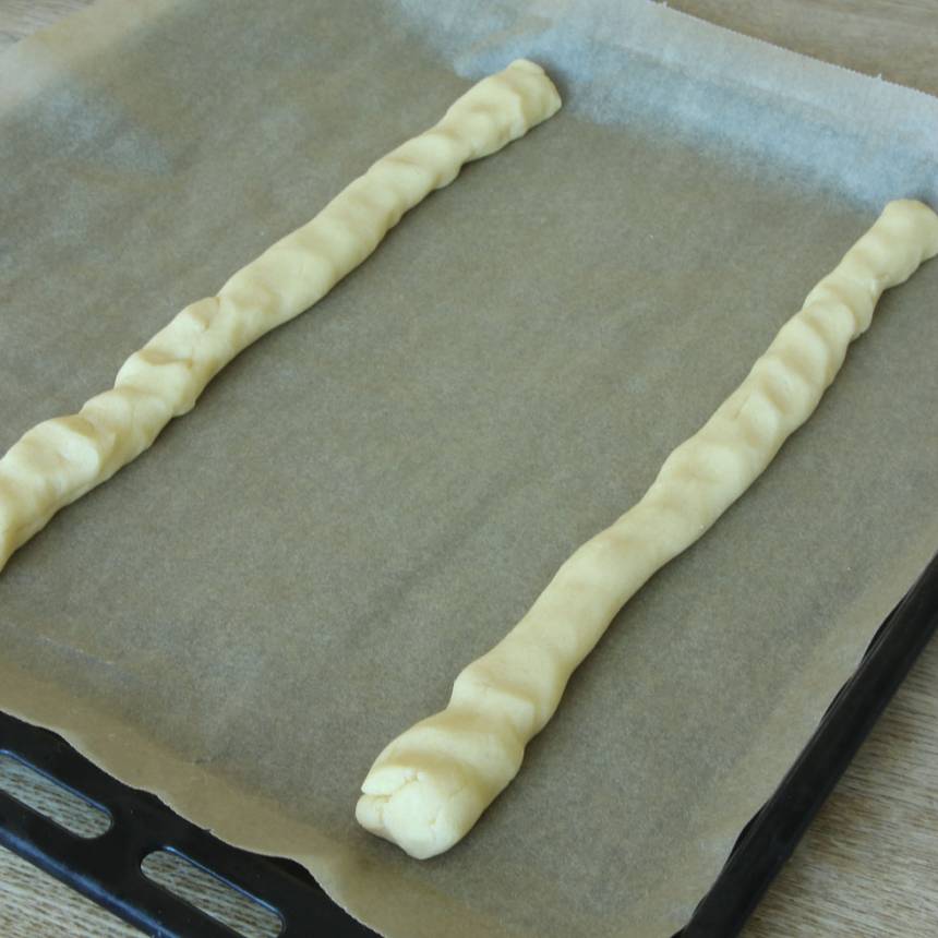 2. Dela degen i två delar och rulla dem till längder, ca 30 cm. Lägg dem brett isär på en plåt med bakplåtspapper. Platta till dem något.