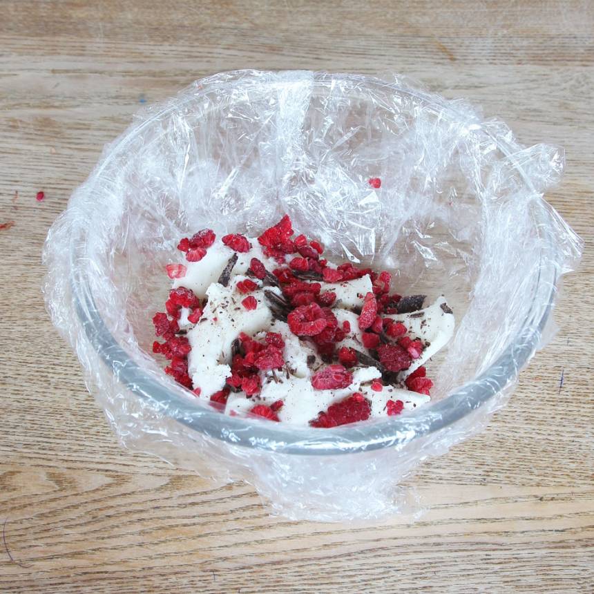 2. Klä en skål med plastfolie. Tryck ner lite glass i botten. Strö över 1/3 av hallonen och chokladen.