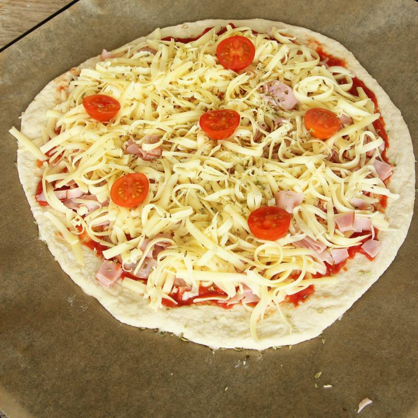 3. Lägg bakplåtspappret med rundeln på en ugnsplåt. Bred ut pizzasåsen på degen. Strö över skinka, riven ost, cocktailtomater och oregano (eller valfri fyllning). Låt pizzan jäsa under bakduk i ca 20 min. Sätt ugnen på 250 grader varmluft.