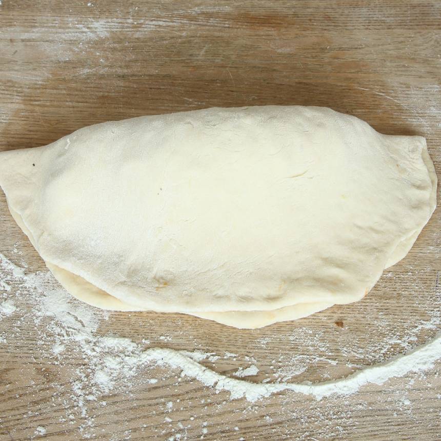 4. Vik ihop pizzan på mitten genom att lyfta upp pappret och lägga det över pizzan. Nyp ihop kanterna ordentligt så fyllningen inte läcker ut. Låt pizzan jäsa på en plåt, under bakduk i ca 20 min. Sätt ugnen på 250 grader varmluft.
