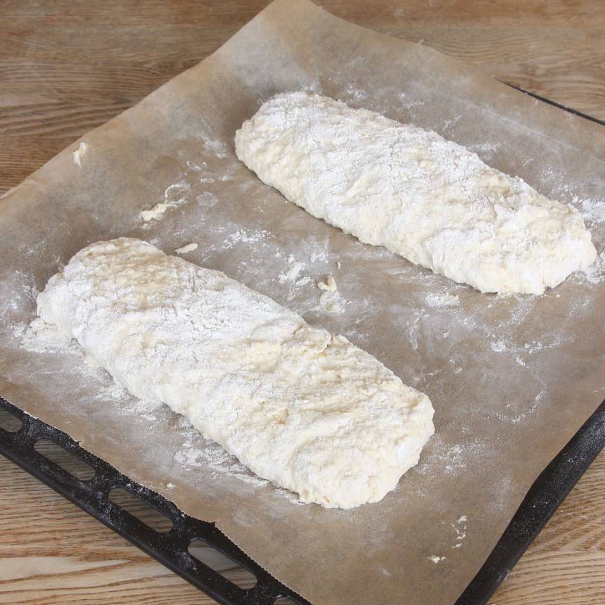2. Ta upp halva den kladdiga degen med mjölade händer. Forma den till en limpa på en plåt med bakplåtspapper. Gör likadant med den andra halvan av degen. Obs! Använd mjölade händer så degen inte fastnar i händerna. Den ska vara kladdig.