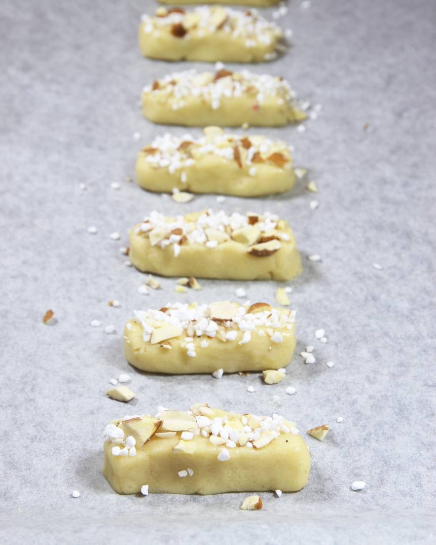 5. Pensla kakorna med äggvita och strö över mandel- och pärlsockerblandningen.