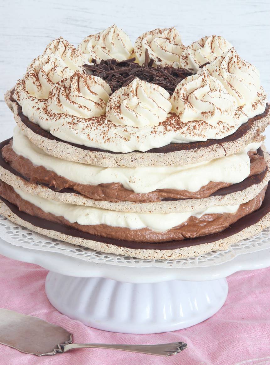 8. Lägg på den sista bottnen. Vispa grädden till garneringen. Bred ut den på toppen, spritsa några toppar, pudra över lite kakao och strö hackad choklad i mitten.