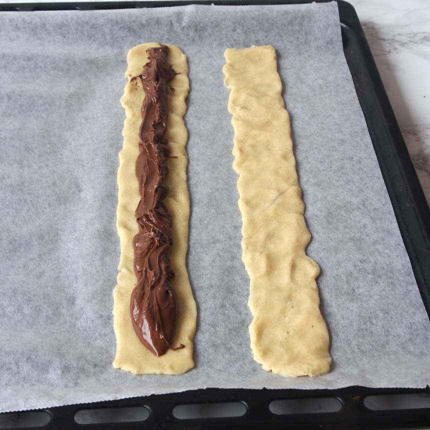 2. Rulla ut degen till fyra rullar, ca 25 cm långa, på en plåt med bakplåtspapper. Platta till dem. Ringla Nutella i mitten på två av längderna. Lägg på de andra längderna som lock. Tryck ihop kanterna.
