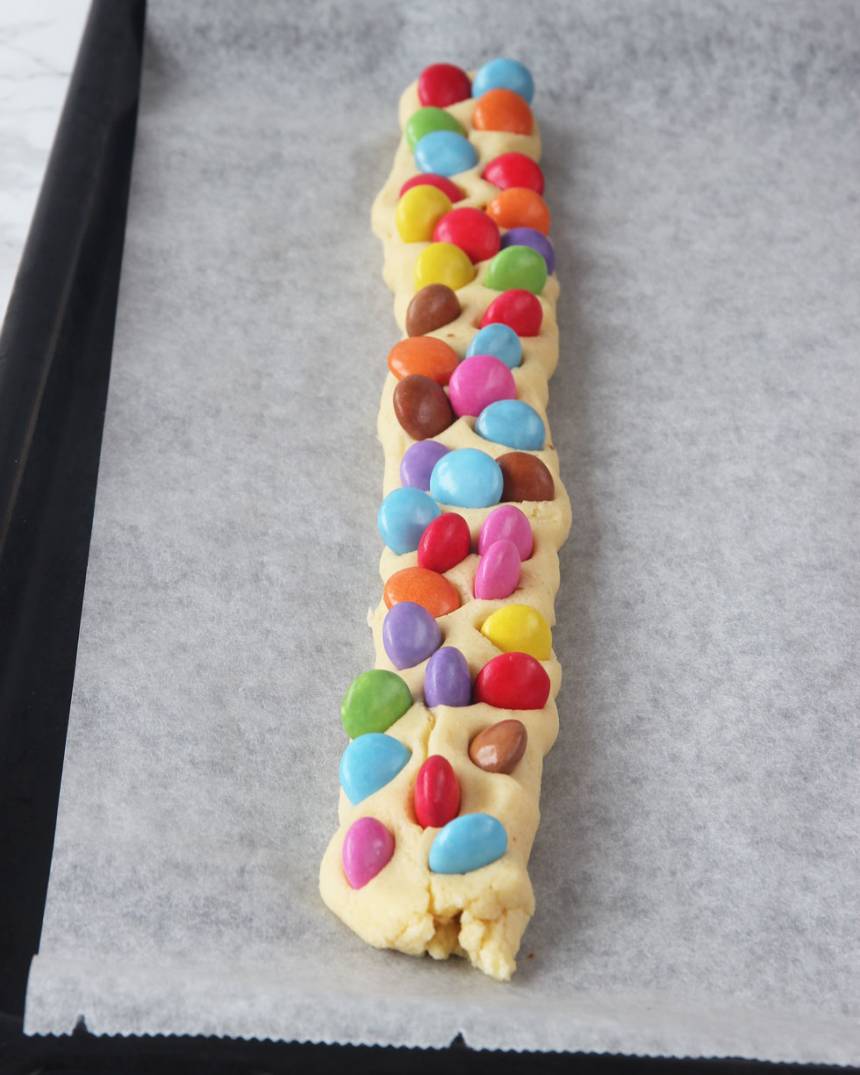 3. Rulla ut längder av degbitarna, ca 25 cm långa. Platta till dem lite. Tryck ner Smarties i degen.